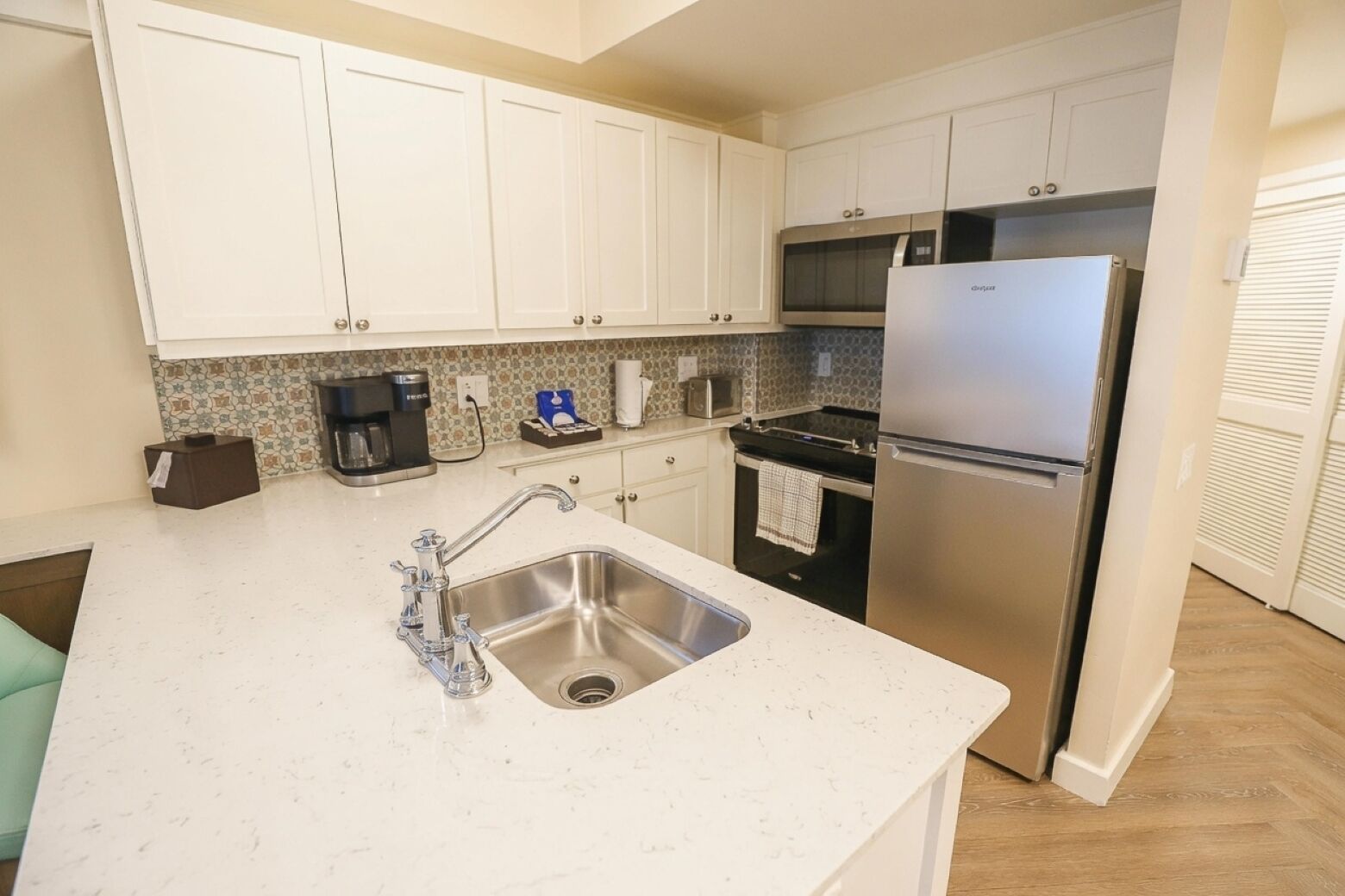 A kitchen with white cabinets, a stainless steel sink, a built-in oven, and a refrigerator.