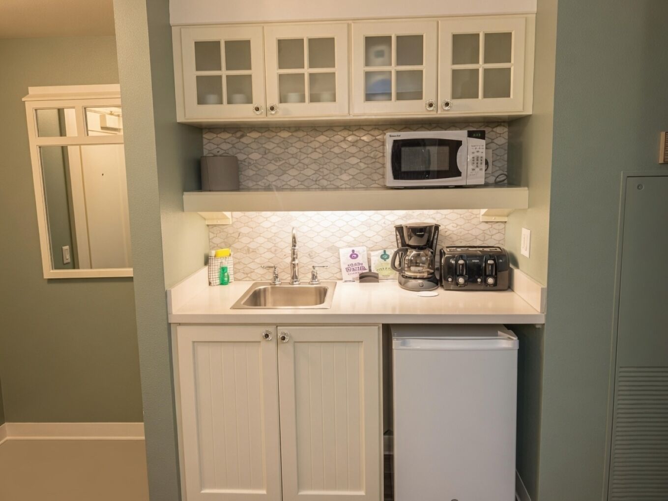 A compact kitchen with white cabinets, a microwave, a coffee maker, and a toaster.