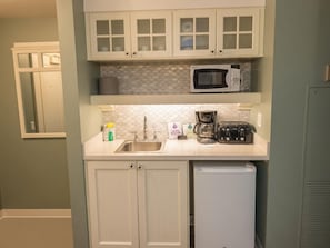A compact kitchen with white cabinets, a microwave, a coffee maker, and a toaster. - Orlando | Lively Group Stay | Pool + Walkable BoardWalk | 2BR Lock-Off (Lake Buena Vista)