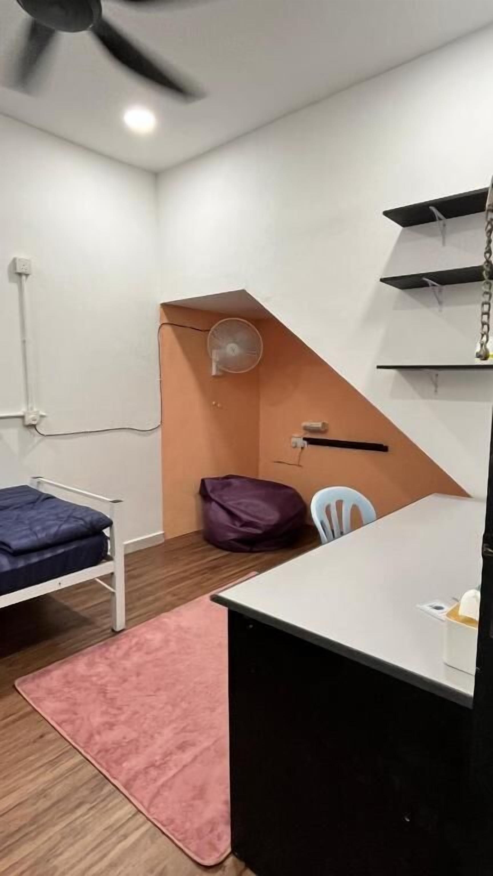 A compact room with a bunk bed, a desk, a chair, a fan, and a small shelf unit.