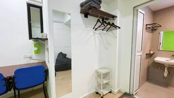A compact room with a desk, chair, mirror, and a small white shelf.