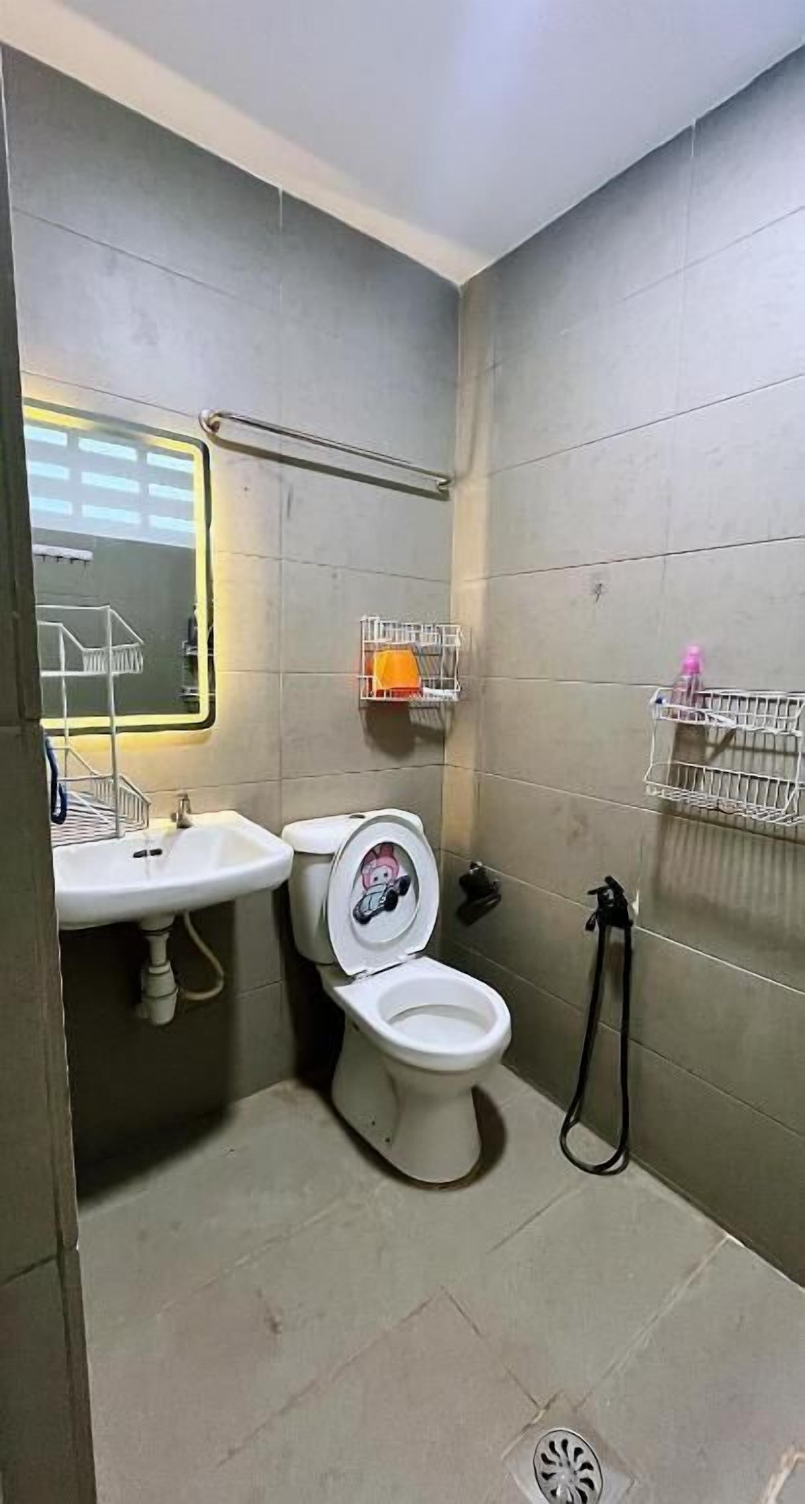 Baño pequeño con inodoro, lavamanos y espejo. Hay repisas para guardar cosas en la pared y una zona de ducha.