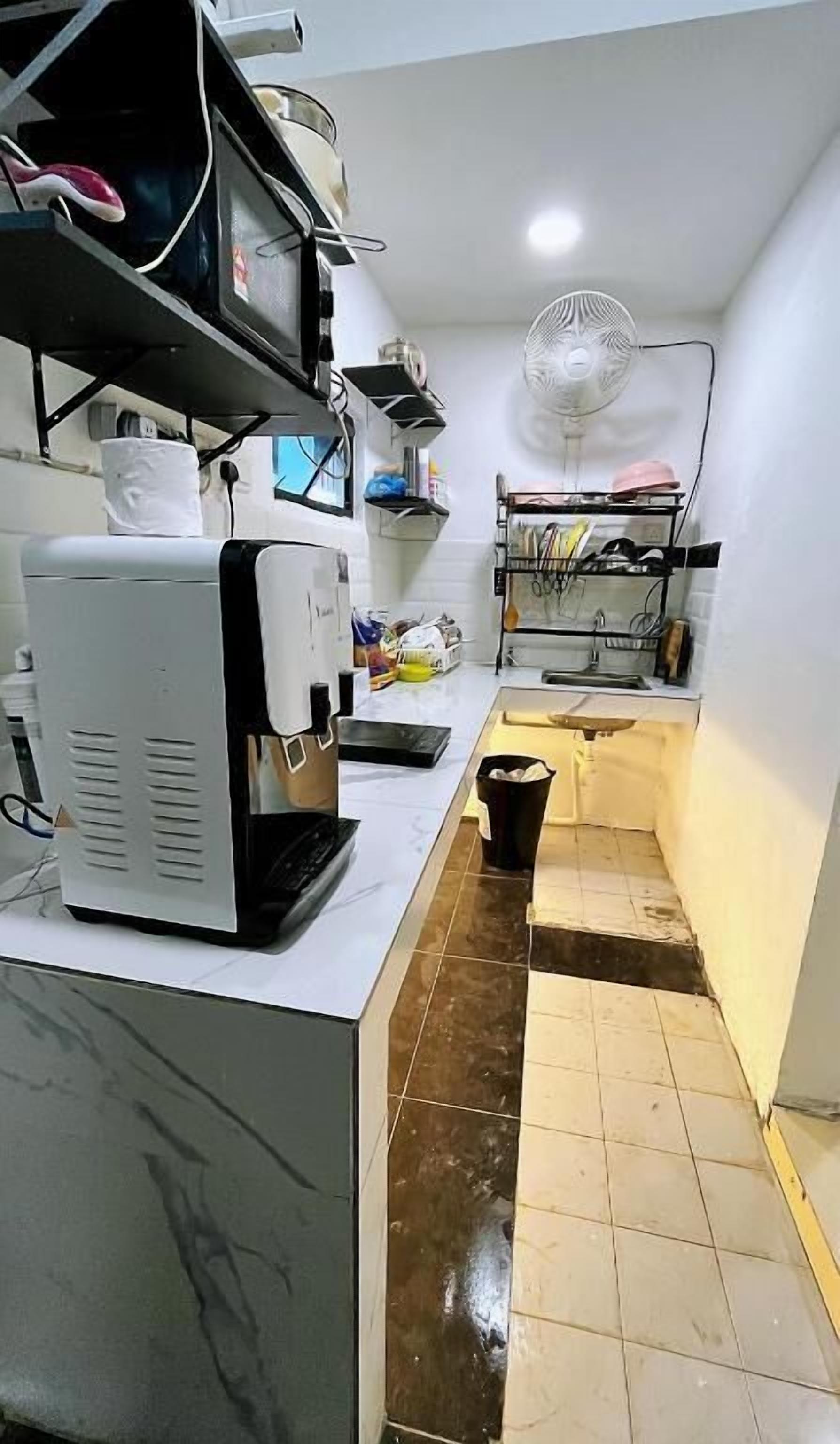A compact kitchen with a coffee maker, a fan, and a small sink.