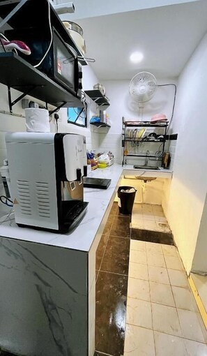 A compact kitchen with a coffee maker, a fan, and a small sink.