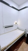 A small, single-bed room with a white mattress, a headboard with a light fixture, and a radiator below.