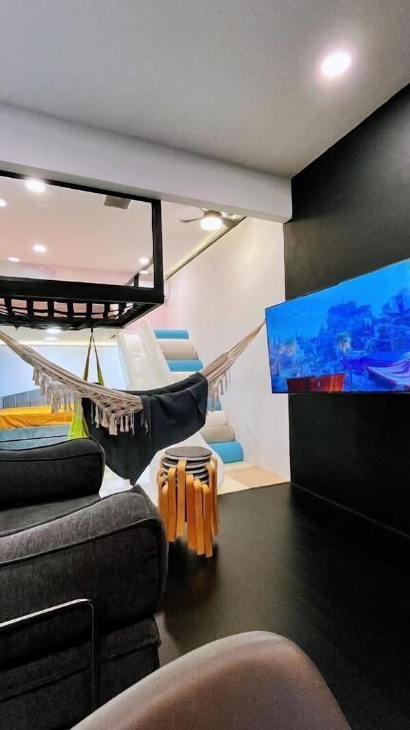 A modern living room with a large flat-screen TV mounted on the wall, a hammock, and a sofa.