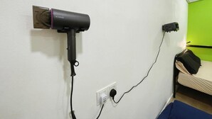 A room with a bed, a power outlet, and a black device plugged in.