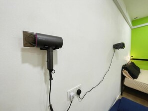 Una habitación con una cama, un enchufe y un dispositivo negro conectado.
