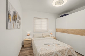 A bedroom with a bed, bedside lamps, a window with blinds, a ceiling light, and a wall-mounted artwork.
