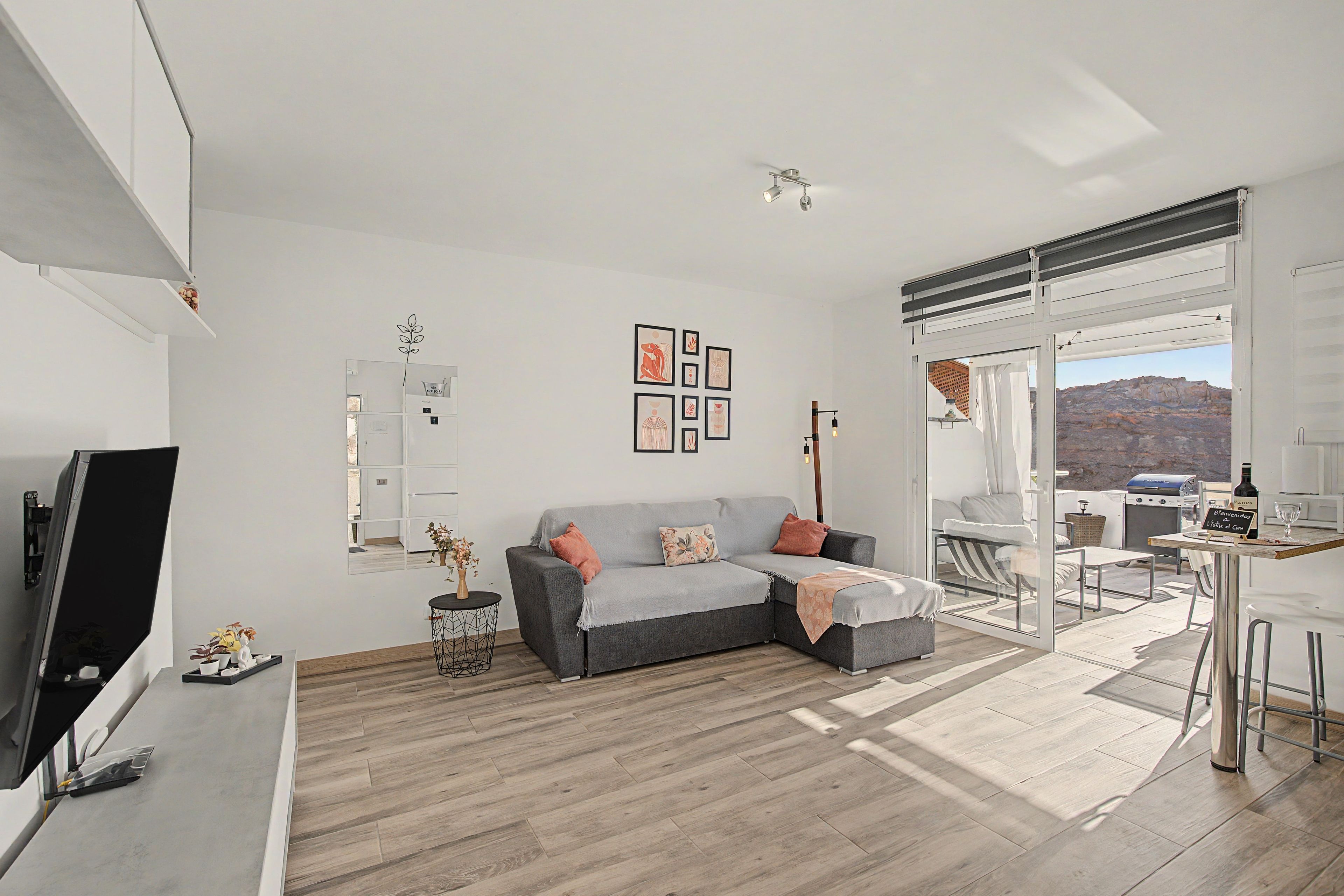 Una sala de estar moderna con un sofá gris, un televisor de pantalla plana y un comedor con mesa y sillas.