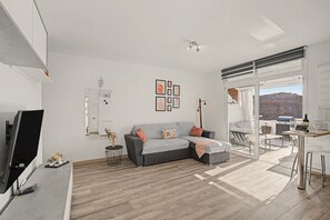 A modern living room with a grey sofa, a flat-screen TV, and a dining area with a table and chairs.