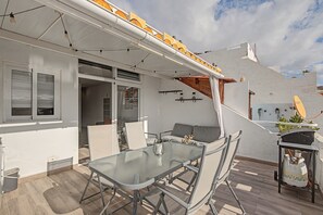 A rooftop terrace with a glass table and chairs, a sofa, and a satellite dish.