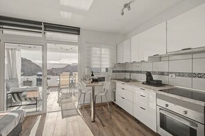 A modern kitchen with a view of mountains, a dining area with a table and chairs, and a large oven. - Views of Playa del Cura with Fantastic Terrace (Mogán)