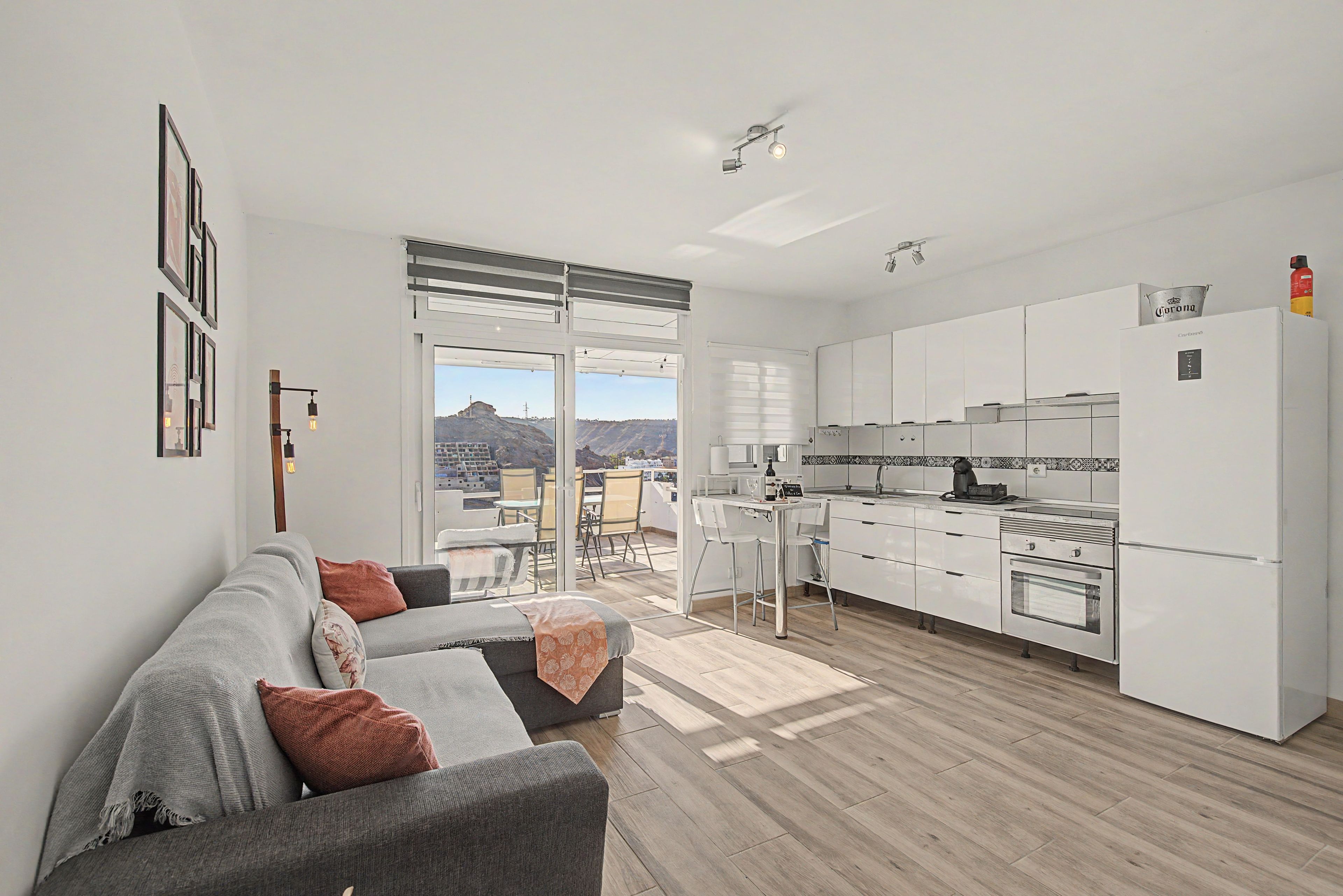 A modern apartment with a living area, kitchen, and a balcony with a city view.