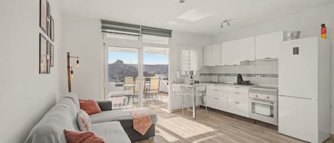 A modern apartment with a living area, kitchen, and a balcony with a city view.