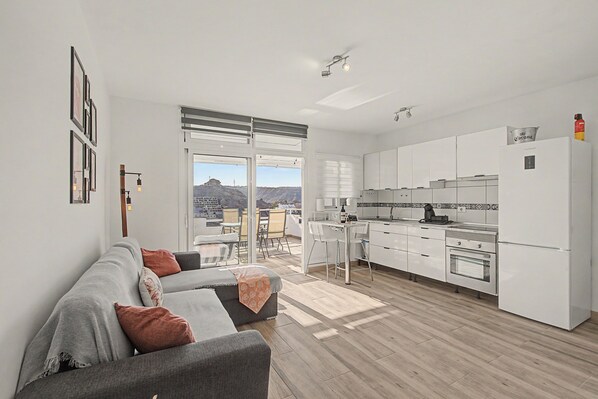 A modern apartment with a living area, kitchen, and a balcony with a city view.