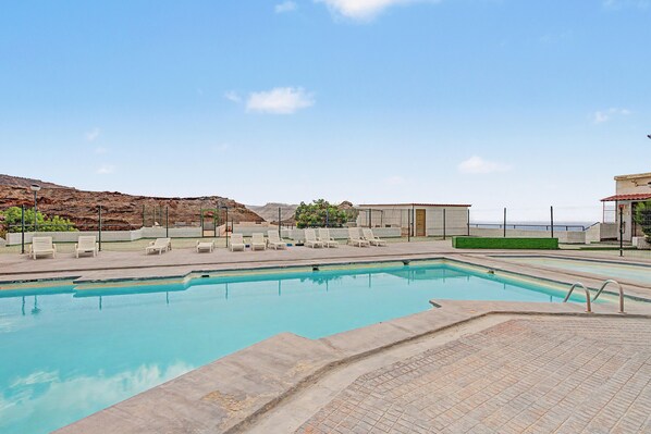 A swimming pool with a clear blue water surface, surrounded by a paved deck area with several lounge chairs.