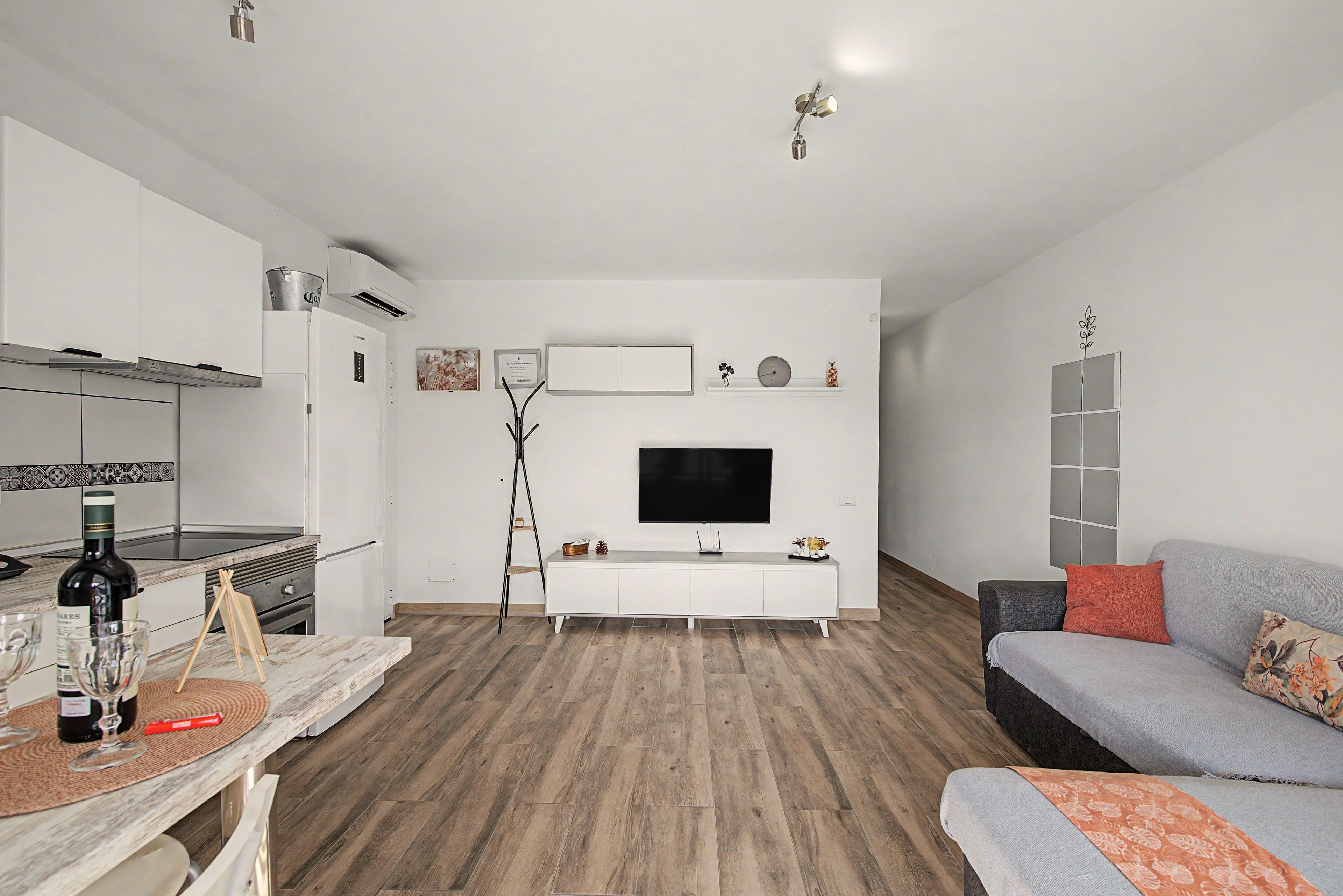 Una sala moderna con televisor de pantalla plana, un sofá, un comedor con mesa y una cocina con armarios blancos.