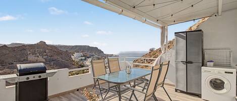 Un balcón con mesa y sillas, una parrilla, lavadora y vistas al litoral.