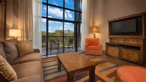 Ein Wohnzimmer mit einer Couch, einem Sessel, einem Fernseher und einem Balkon mit Sitzgelegenheiten.