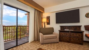 Een hotelkamer met balkon, een bank, een televisie en een houten kast.