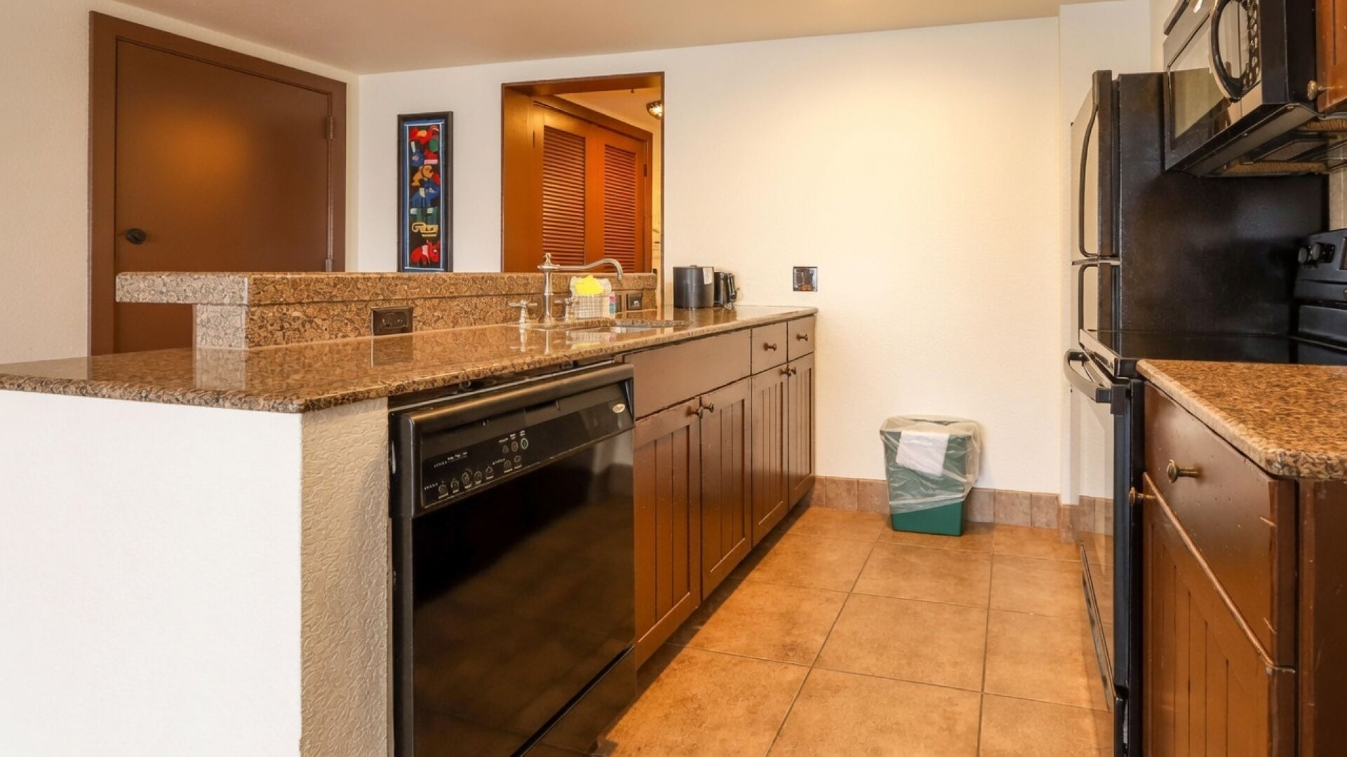 Una cocina con lavavajillas, horno y cubo de basura.