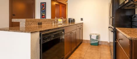 Una cocina con lavavajillas, horno y cubo de basura.