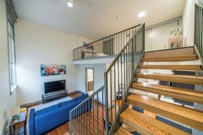 Ein modernes Wohnzimmer mit Flachbildfernseher, einem blauen Sofa und einer Treppe, die zu einer oberen Ebene führt.