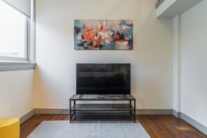 Ein modernes Wohnzimmer mit einem Flachbildfernseher auf einem Metallständer, einem Bild an der Wand und einem Holzboden.