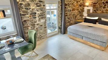 Un dormitorio con pared de piedra, una cama, una mesa de comedor con sillas y vistas a través de una puerta.