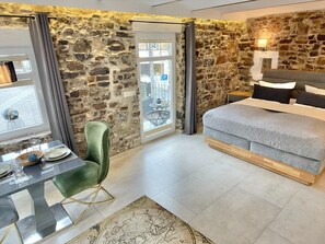 Un dormitorio con pared de piedra, una cama, una mesa de comedor con sillas y vistas a través de una puerta.