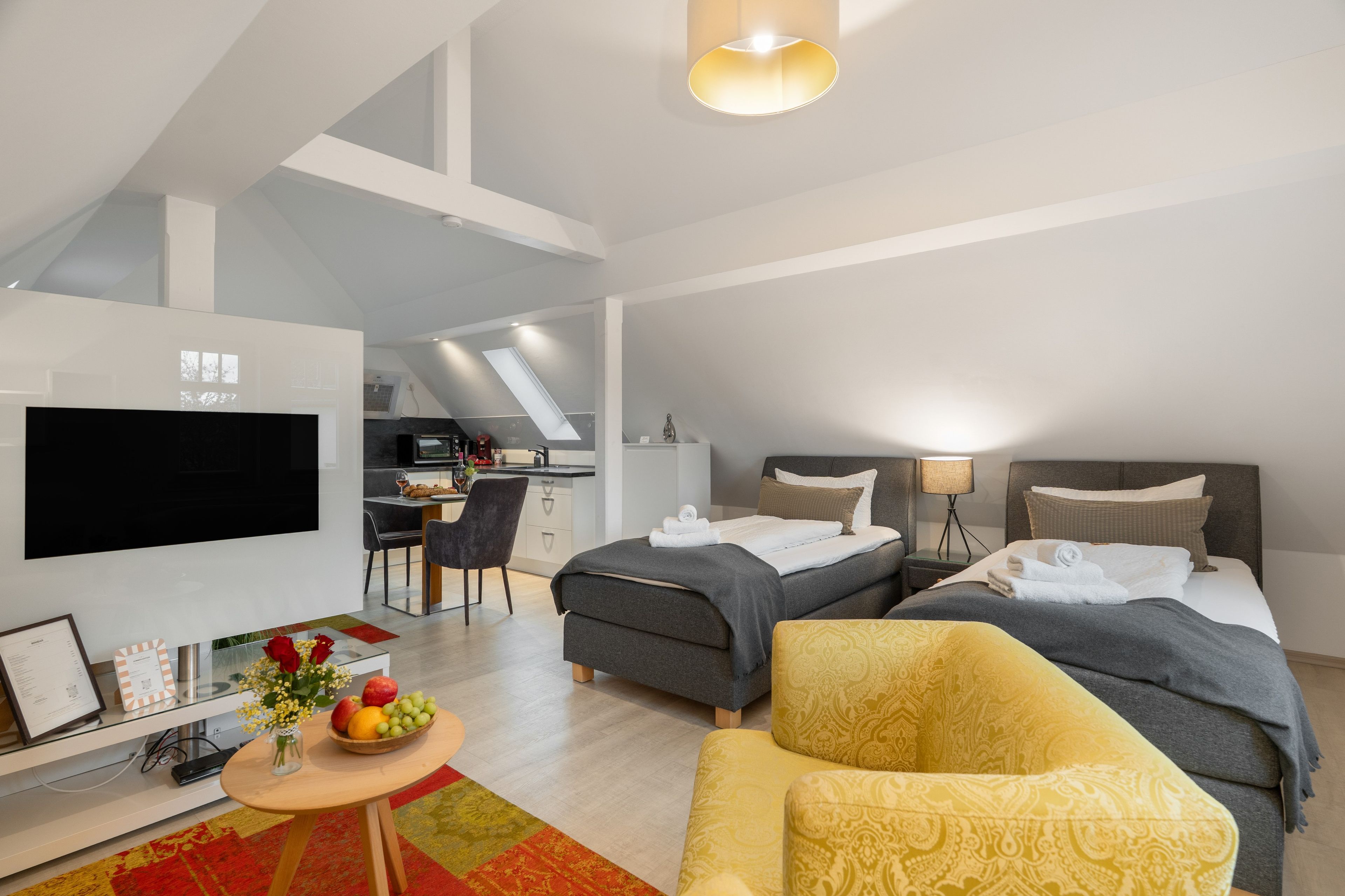 A modern hotel room with a flat-screen TV, a dining area, and a bed with two pillows.