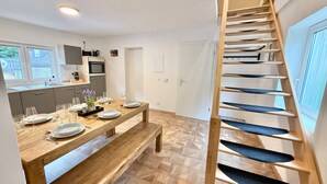 A modern kitchen with a wooden dining table set for four, a staircase with blue steps, and a view of the outside. - Vetera Apartment with Mountain View, Private Terrace & Wi-Fi (Bendorf)