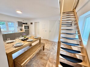 A modern kitchen with a wooden dining table set for four, a staircase with blue steps, and a view of the outside. - Vetera Apartment with Mountain View, Private Terrace & Wi-Fi (Bendorf)