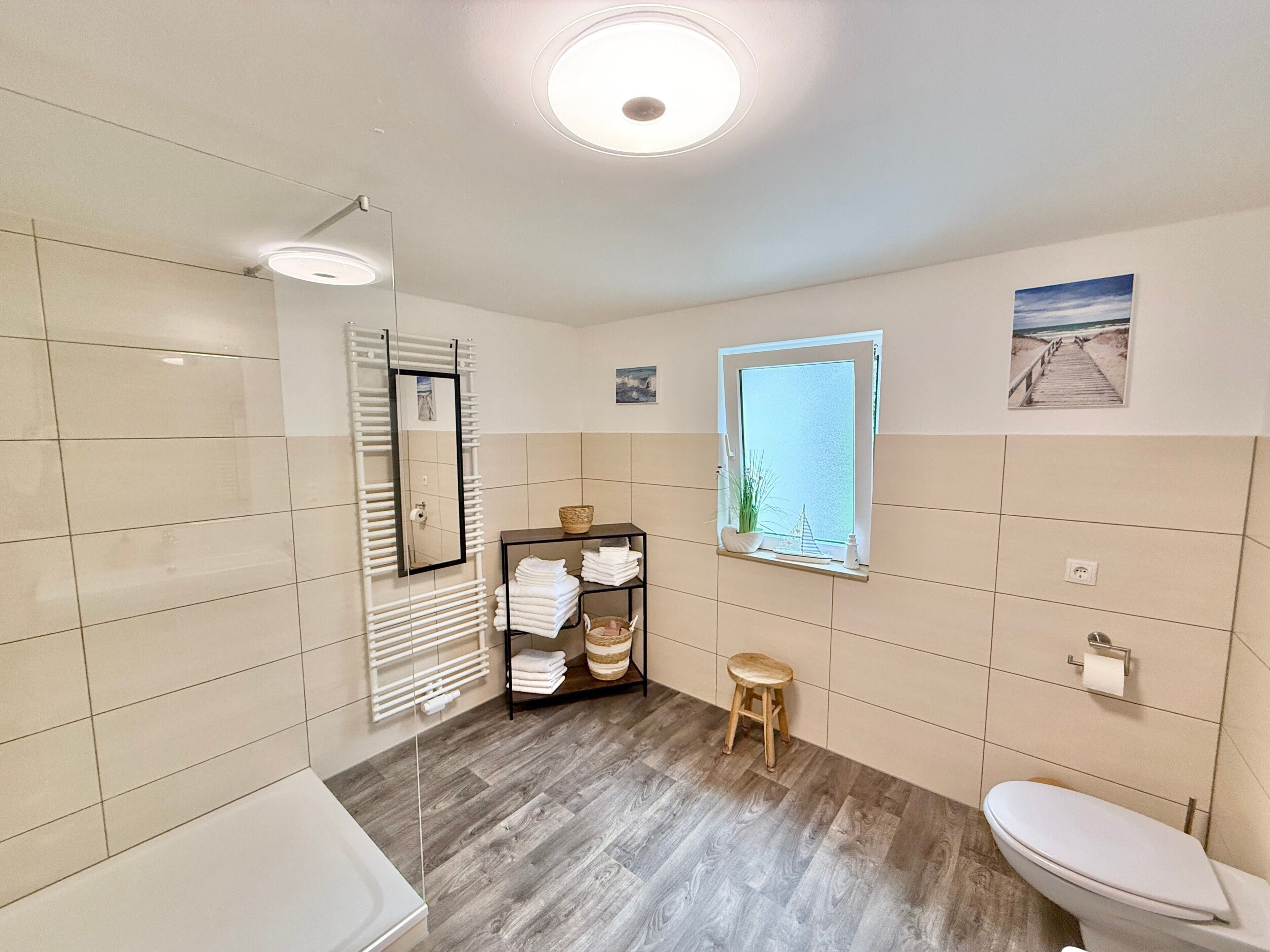 Une salle de bain avec un plancher en bois, des toilettes blanches, un porte-serviettes et une fenêtre donnant sur un beau paysage.