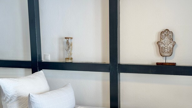 A bed with white bedding and pillows, a small decorative item on the bed, and a wall with a black beam and a decorative wall piece. - Vetera Apartment with Mountain View, Private Terrace & Wi-Fi (Bendorf)