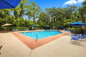 A swimming pool with blue chairs and umbrellas, surrounded by trees. - Serene Villa Steps From Beach w/ Pool and Tennis! (Hilton Head Island)