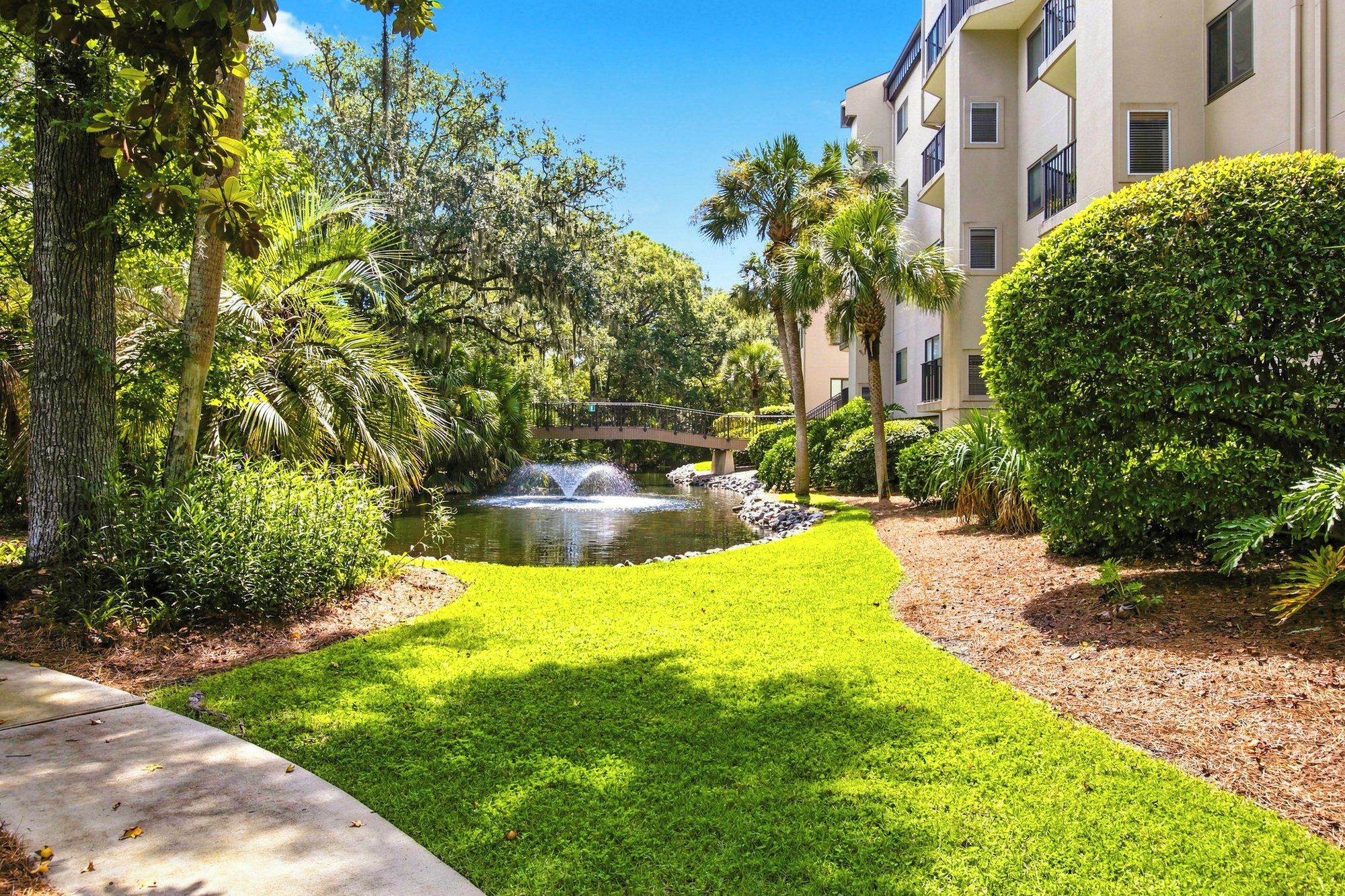 A landscaped garden with a pond, a bridge, and a building with balconies.
