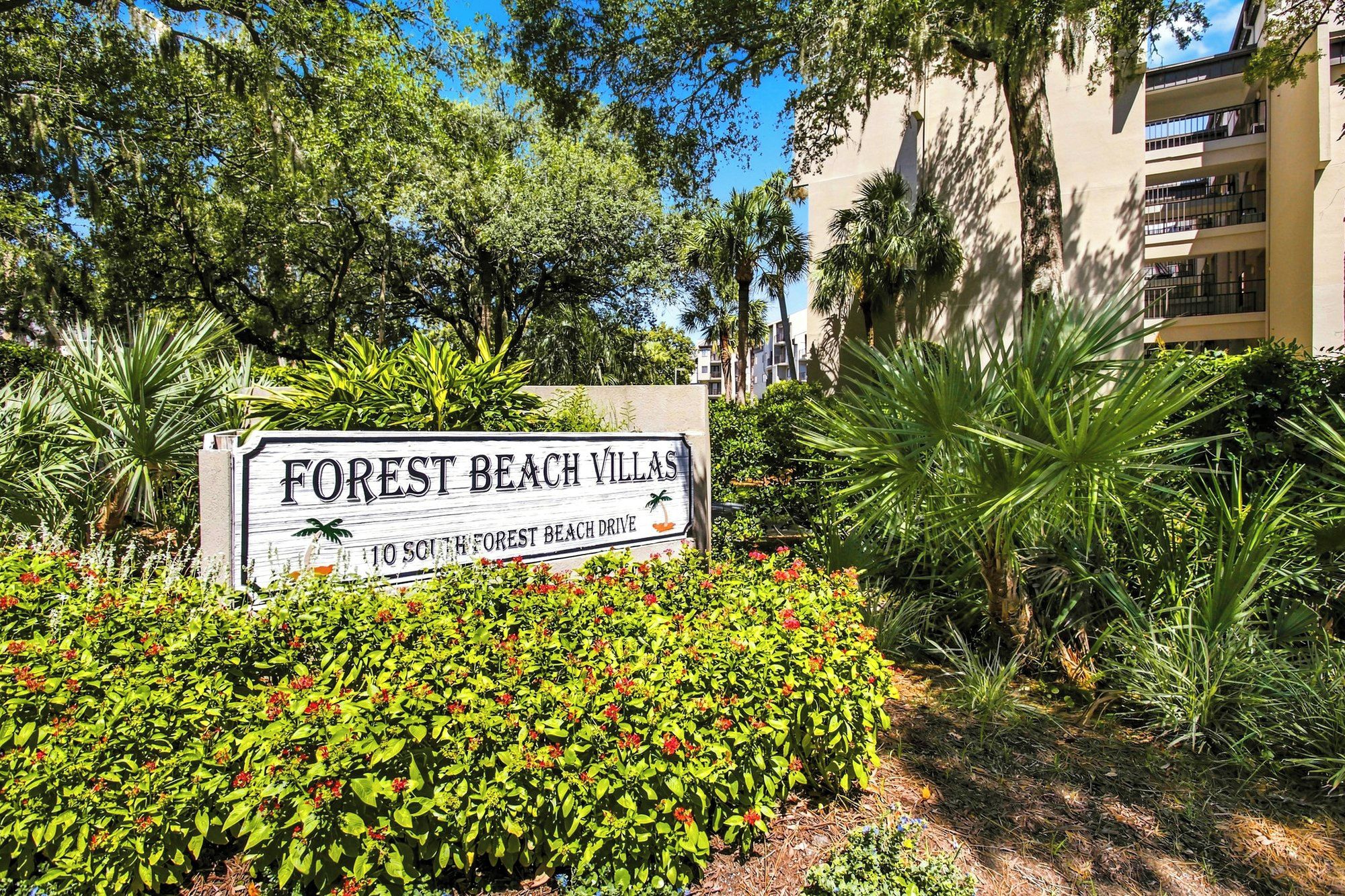 A sign for 'Forest Beach Villas' with a view of lush greenery and a building in the background.
