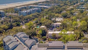 A coastal residential area with multiple apartment buildings, a beach in the background, and a clear sky. - Serene Villa Steps From Beach w/ Pool and Tennis! (Hilton Head Island)