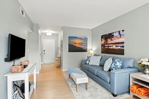 A living room with a flat-screen TV, a sofa with patterned cushions, and two wall-mounted sunset paintings. - Serene Villa Steps From Beach w/ Pool and Tennis! (Hilton Head Island)
