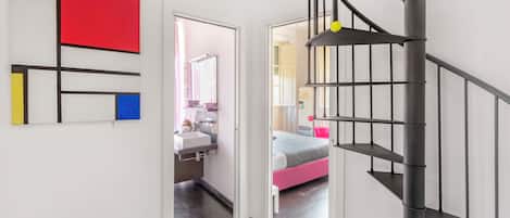 Un intérieur moderne avec un escalier, un couloir menant à une chambre et une salle de bain équipée d’un miroir et d’un lavabo.