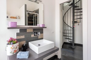 A modern bathroom with a white sink, a mirror, and a black spiral staircase. - Charming two-story apartment located a 15-minute walk from St. Peter's (Roma)
