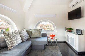 A compact living space with a sofa, a small table with a lamp, a TV, and a view of buildings through a window. - Charming two-story apartment located a 15-minute walk from St. Peter's (Roma)