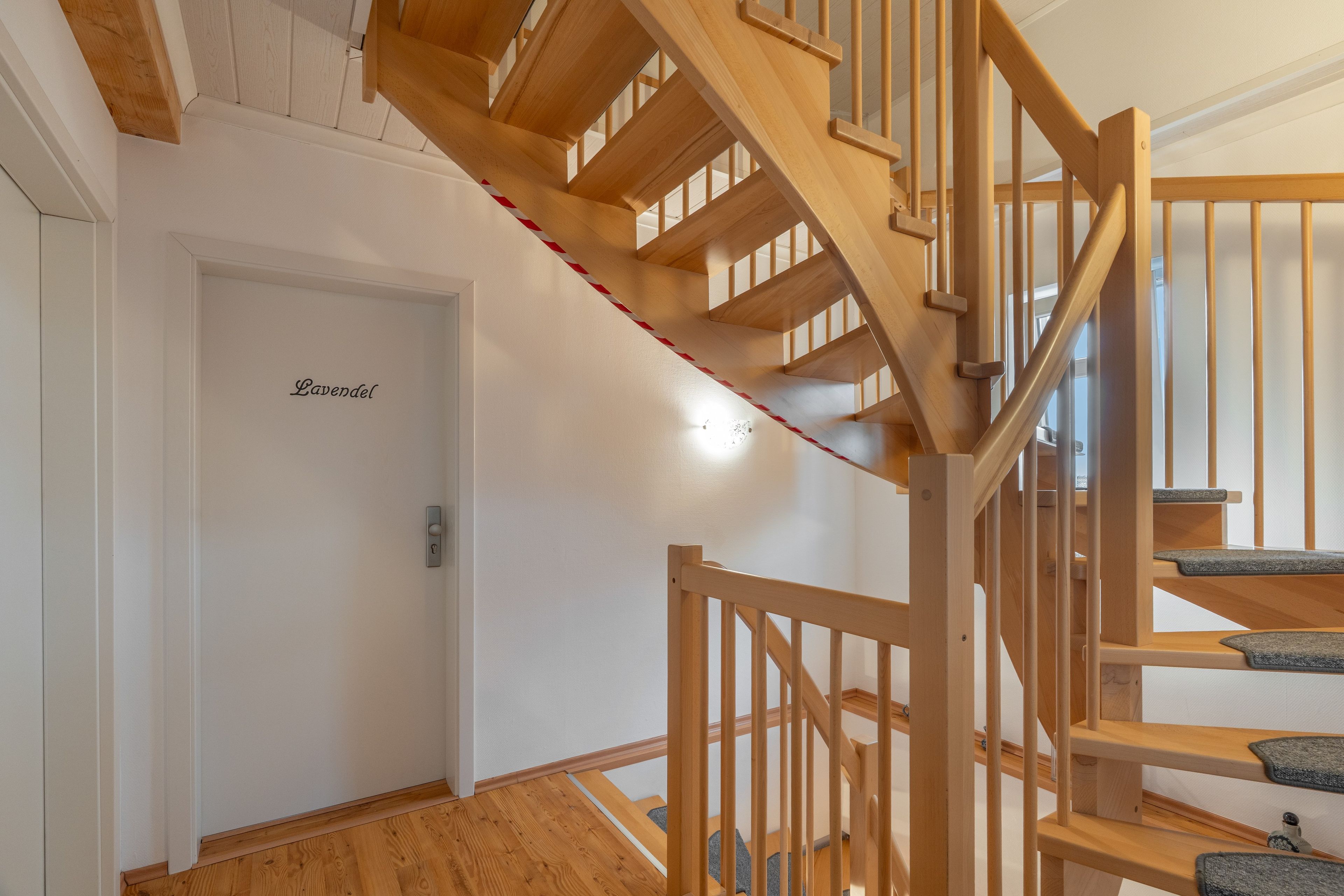 A wooden staircase with a handrail, a door with a nameplate, and a light switch.