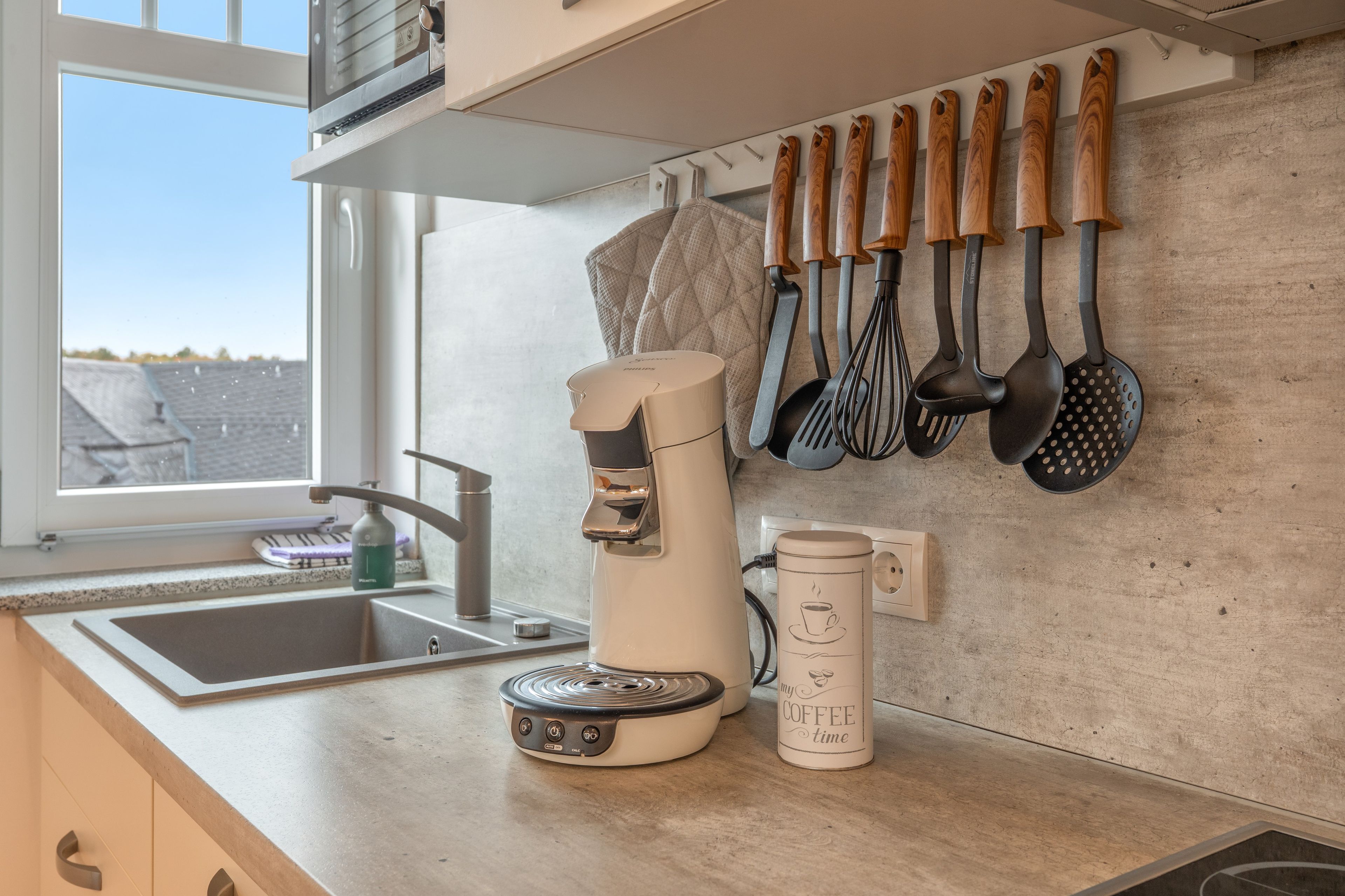 A kitchen with a coffee maker, a kettle, and various utensils on the wall.