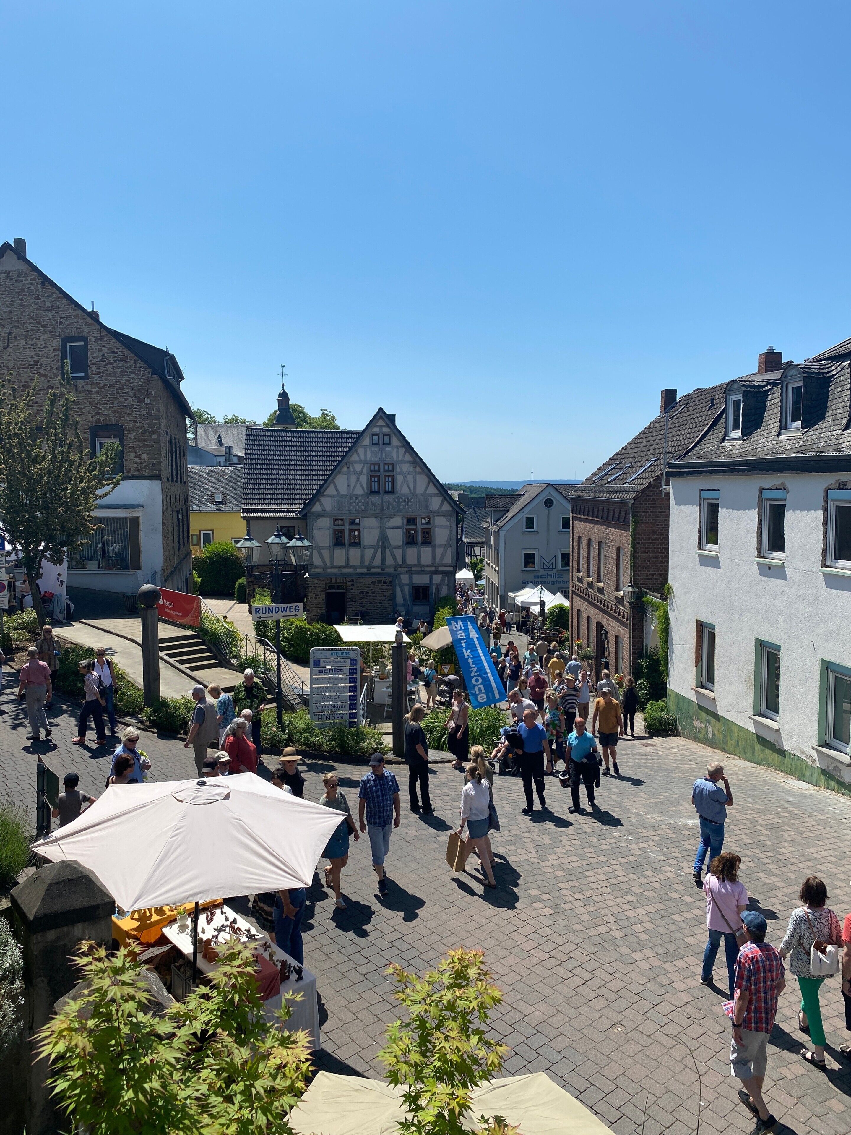 Fußgängerzone mit traditioneller Bebauung, blauem Himmel und Passanten.