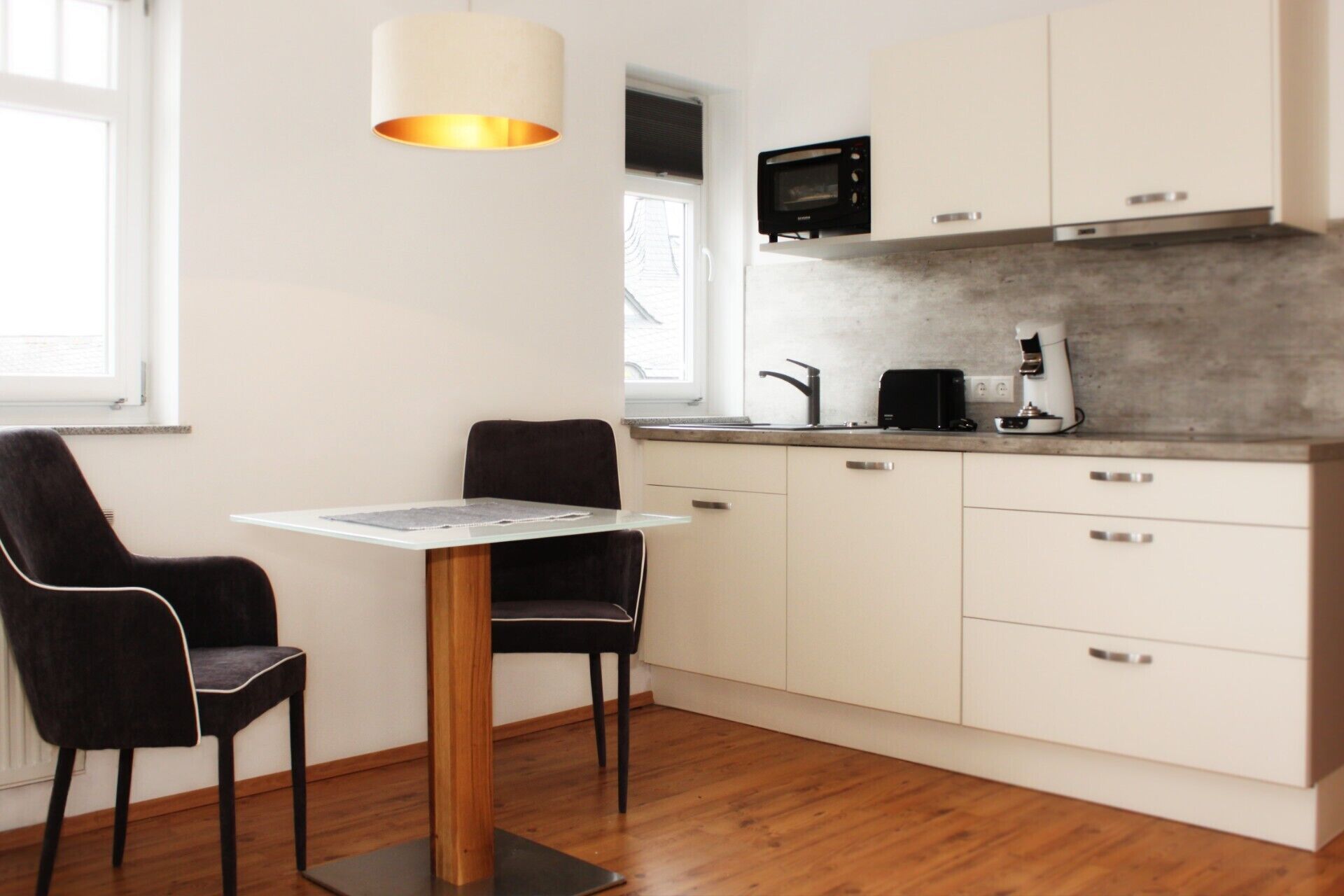 A modern kitchen with a dining table and chairs, a microwave, a coffee maker, and cabinets.