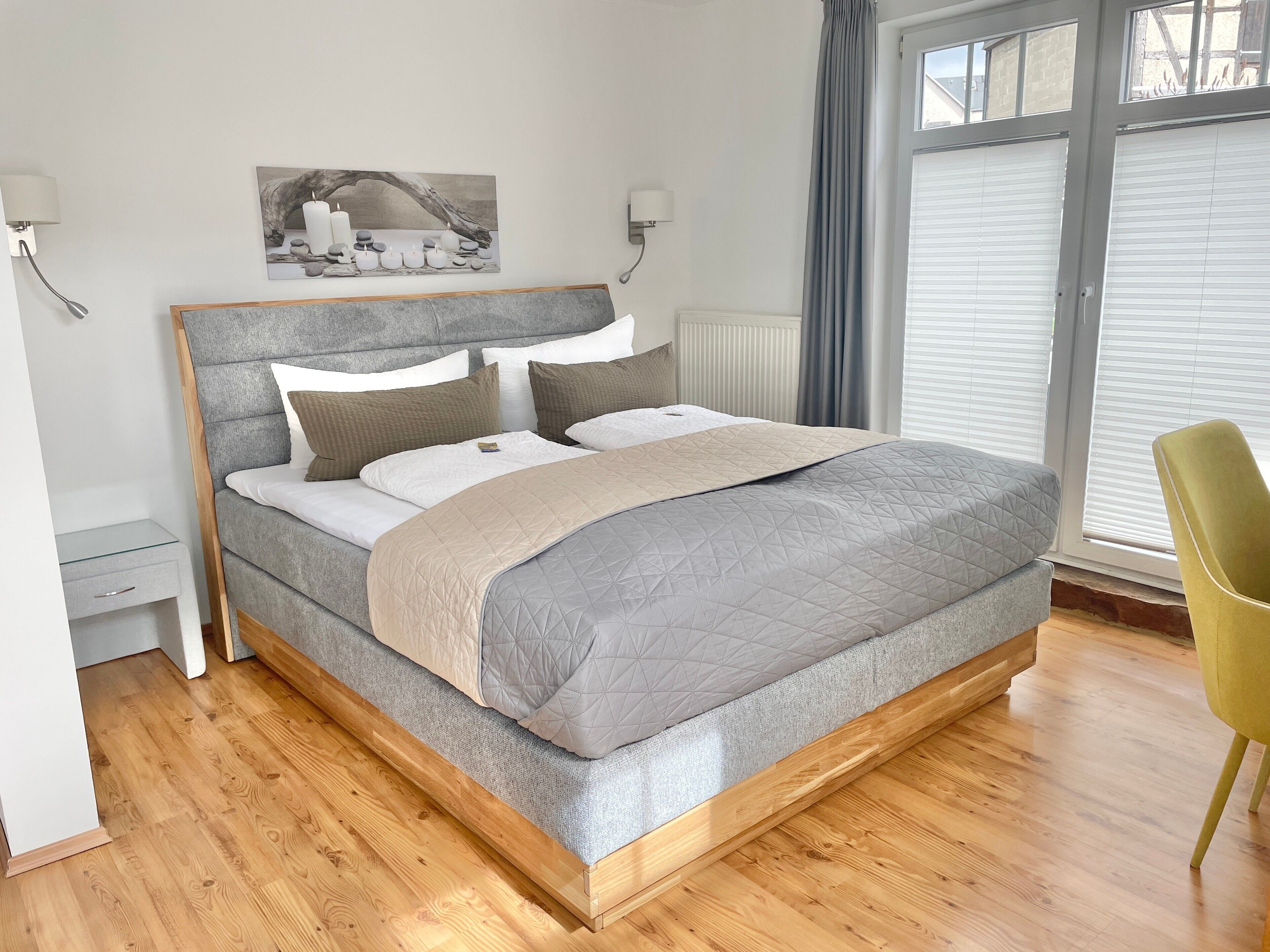Ein modernes Schlafzimmer mit Bett, Nachttischen, einem Sessel und einem Fenster mit Jalousien.