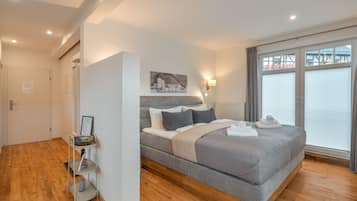 A modern bedroom with a large bed, a bedside table, a wall-mounted light, and a window with blinds.